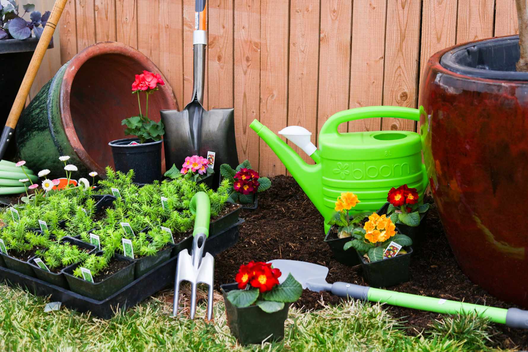 a display of gardening equipment, including a green watering can, shovels, pottery, and multi-colored flowers