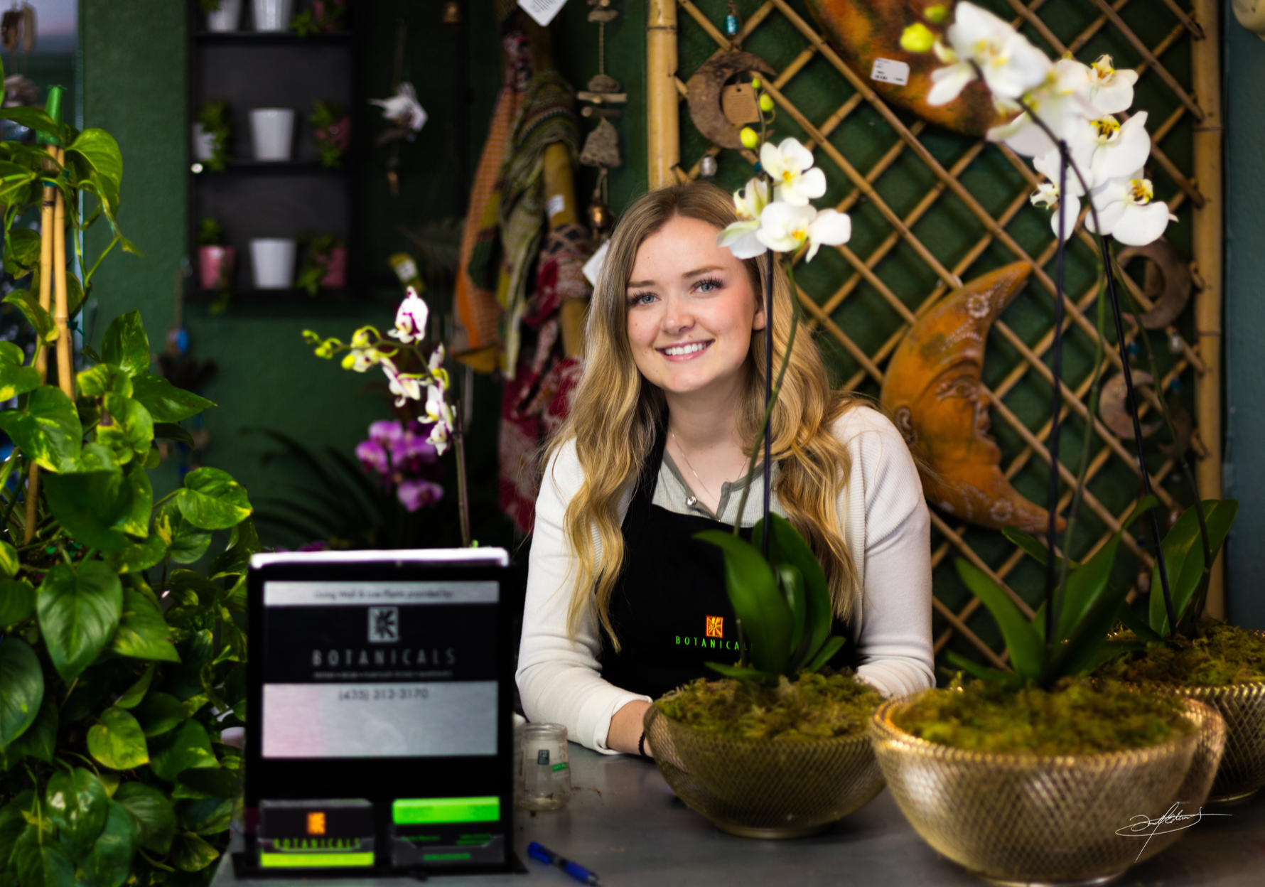 a woman standing and smiling at the counter, surrounded by beautiful plants